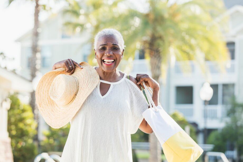 photo of smiling senior woman holding a beach hat and bag