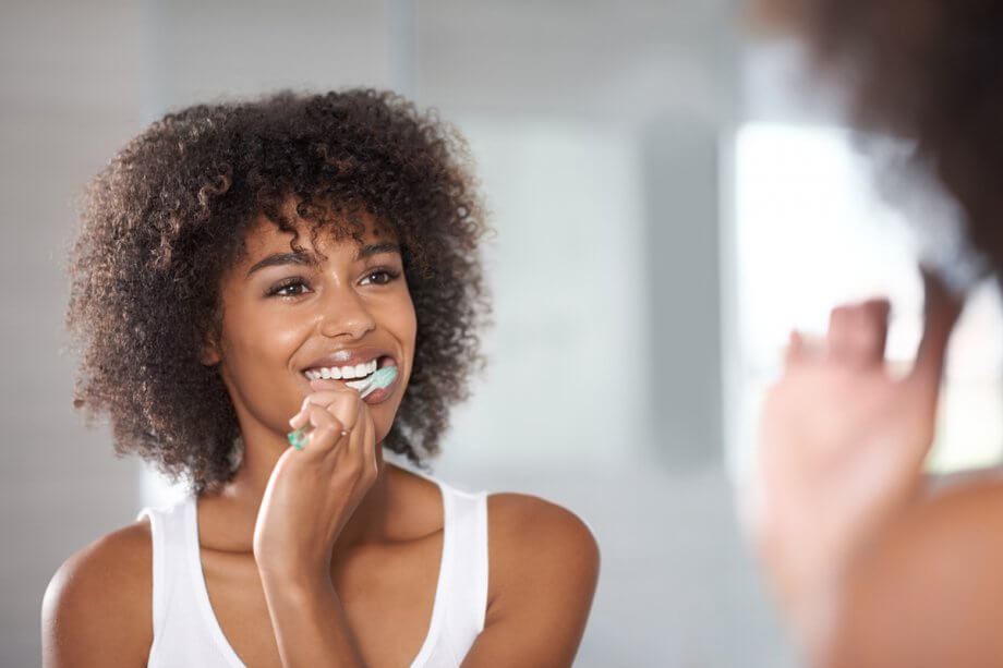 reflection of young woman brushing teeth in bathroom mirror