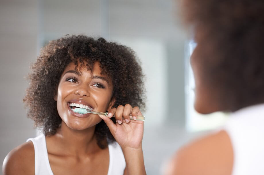 reflection of young woman brushing teeth in bathroom mirror