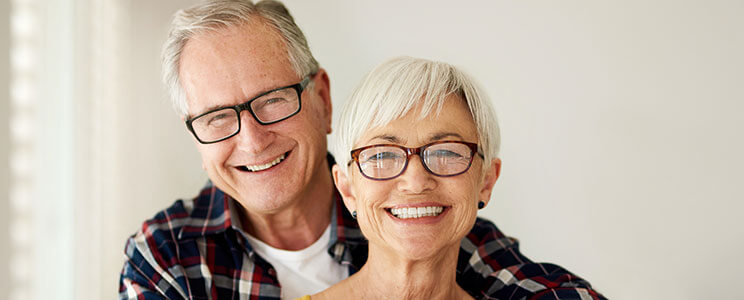 older couple, each wearing dark rimmed glasses, smiling