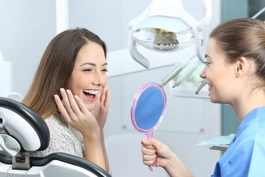 smiling female patient looking in mirror held by dental assistant