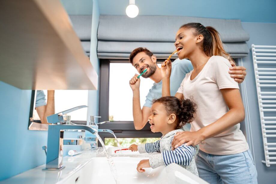 husband, wife and toddler daughter brushing teeth in front of bathroom mirror