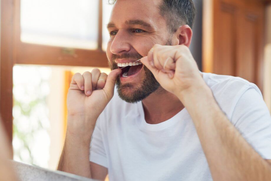 reflection of man flossing in bathroom mirror