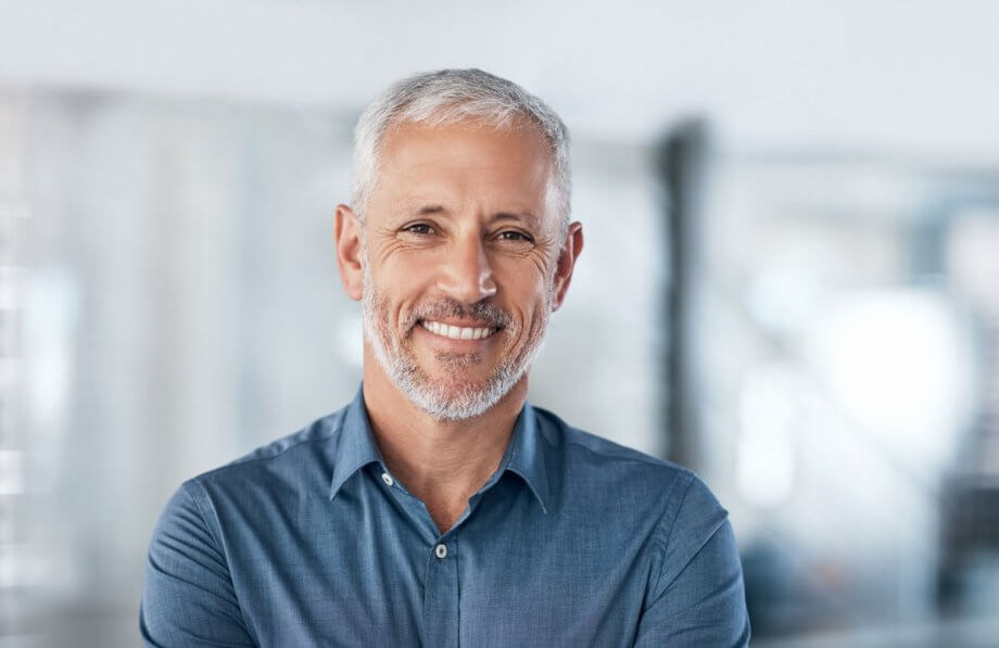 older smiling man with grey hair and beard and blue button-down shirt