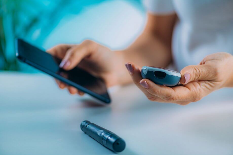 woman's hands holding cell phone and portable glucose monitoring device