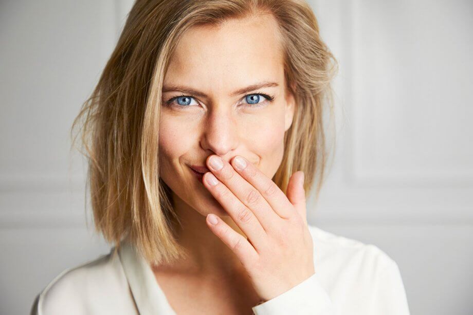 young blonde woman smiling but covering mouth with hand