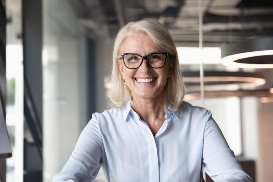 older woman with black framed glasses in office, smiling