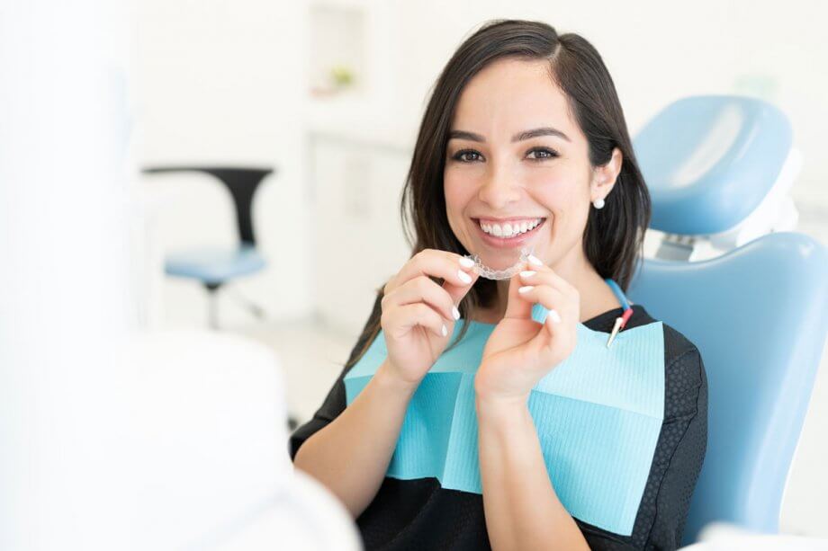 female patient in dental chair smiling, holding invisalign appliance